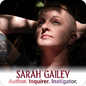 ©Kate Dollarhyde 2023 Headshot Alt Text: Sarah Gailey, a white person with auburn hair, in a rail tunnel. They are wearing red boots, ripped jeans, a black tank top and a black sleeveless hoodie. Their hair is long on top and shaved on the sides. They are running a hand through their hair and resting the opposite elbow on one knee. © Sarah Gailey