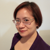Diana Pho, a Vietnamese-American person with straight, chin-length brown hair, in a head-and-shoulders photo. She is wearing silver glasses, silver hoop earrings, a black top, and a purple blazer. She is looking at the camera with a half-smile. 
A headshot of Diano Pho, who is looking at the camera with a half smile.